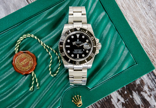 Rolex watch on top of its green presentation case with a seal pendant