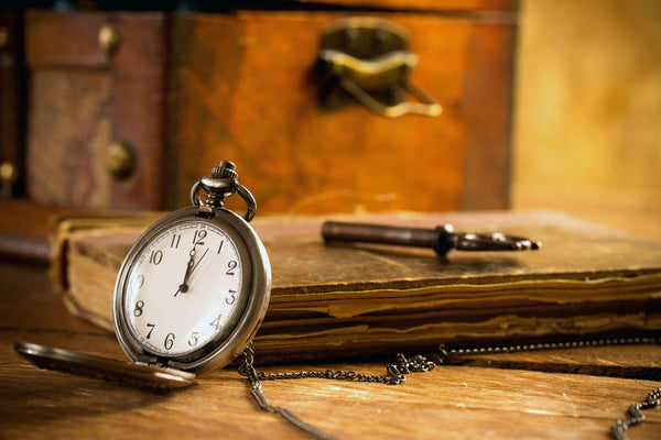 Vintage pocket watch next to an old book and suitcase